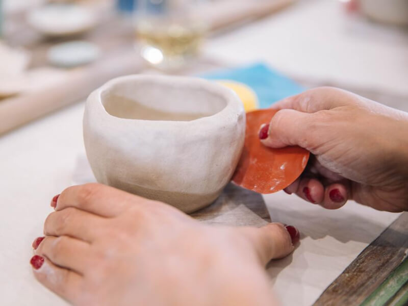 Woman with red painted nails shaping a clay cup